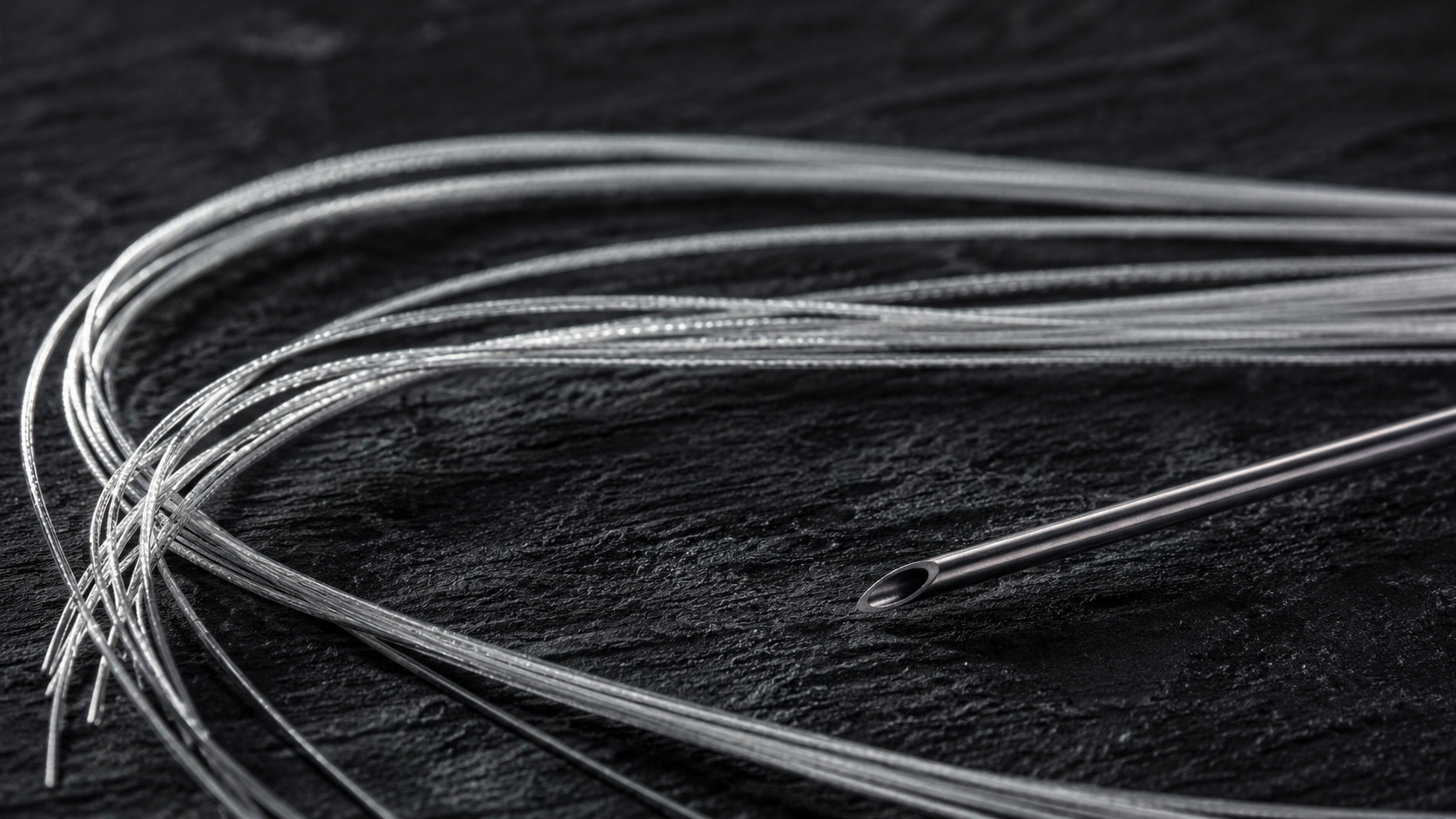 Fine threads beside a needle on a dark surface